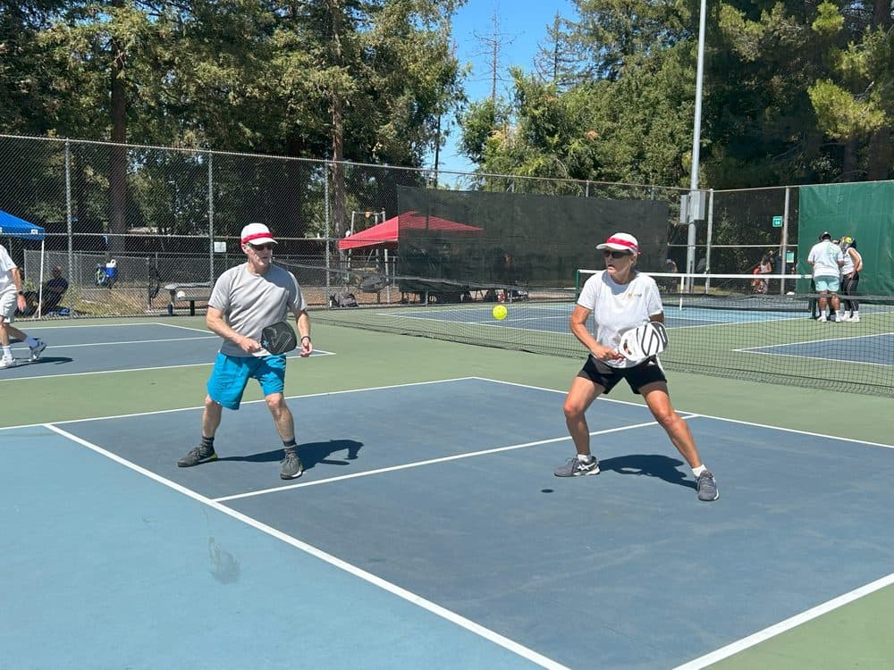 Senior players mid-rally on a converted court